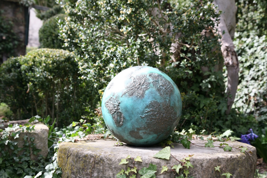 Bronze sphere sculpture in situ on stone pedestal in garden with ivy